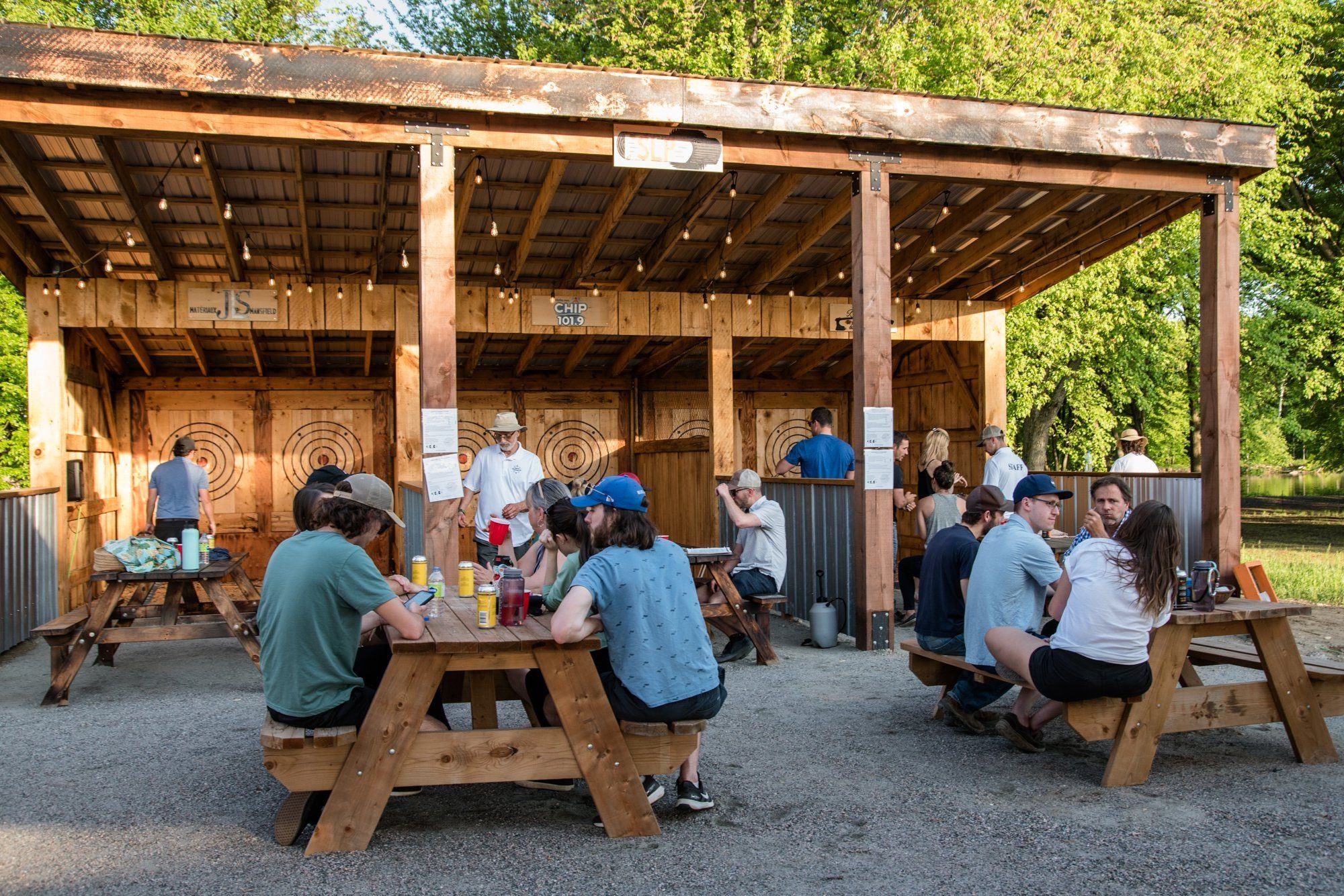 A group seated at picnic tables under the axe throwing pavilion